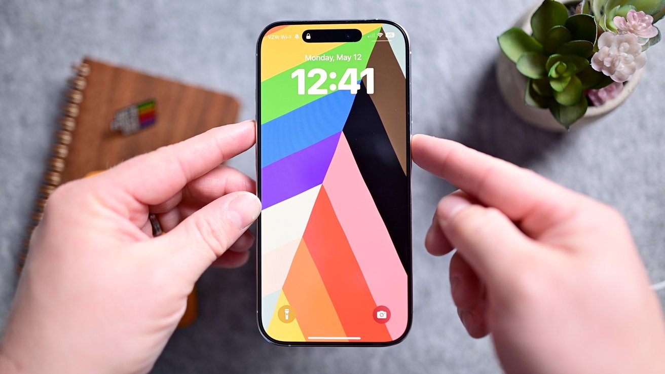 iPhone на сером столе с цветными обоями и временем