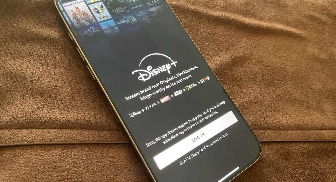 Смартфон на коричневой текстурированной поверхности отображает экран входа в приложение Disney+ с логотипами потоковых сервисов, таких как Pixar, Marvel и Star Wars.